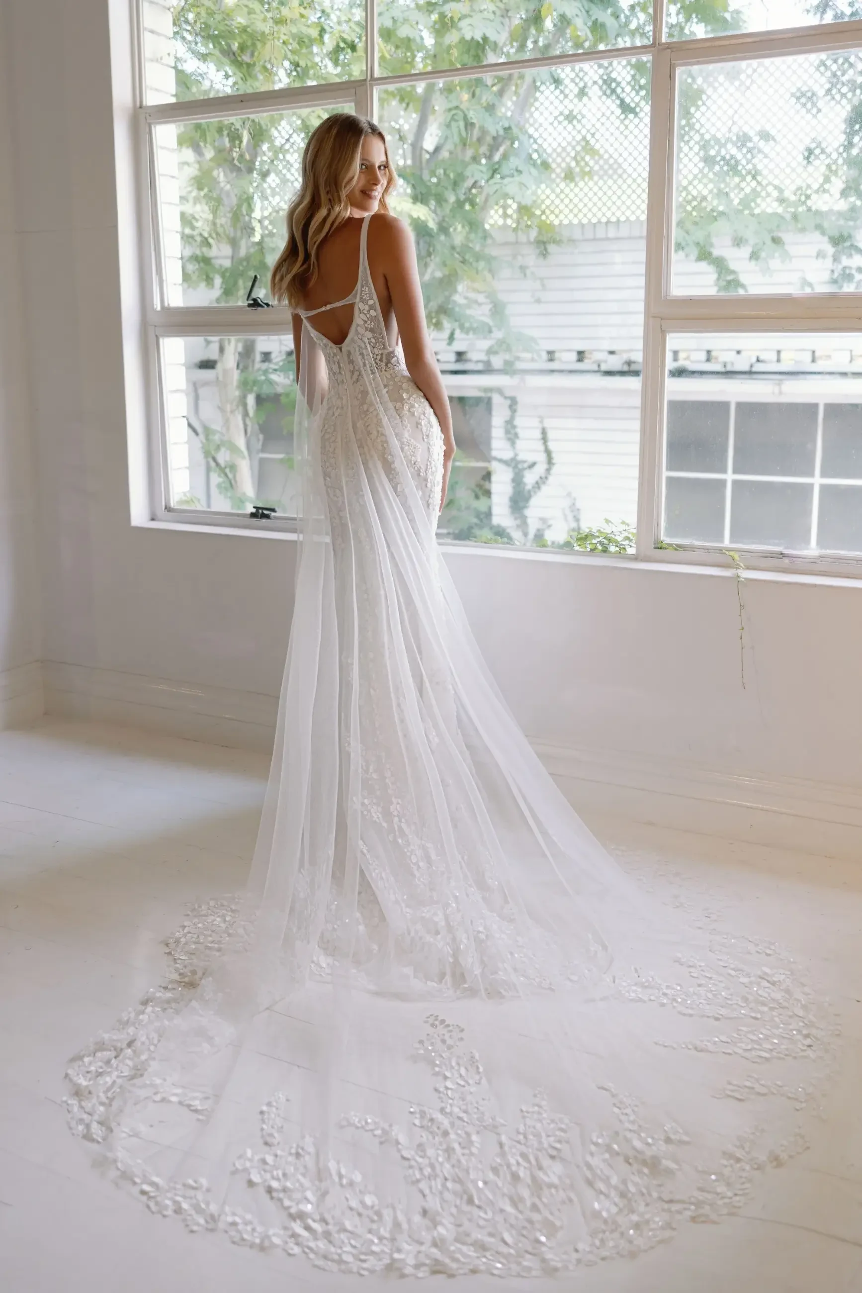 Model is wearing a sleeveless lace fit-and-flare gown featuring a low open back and subtle floral detailing.