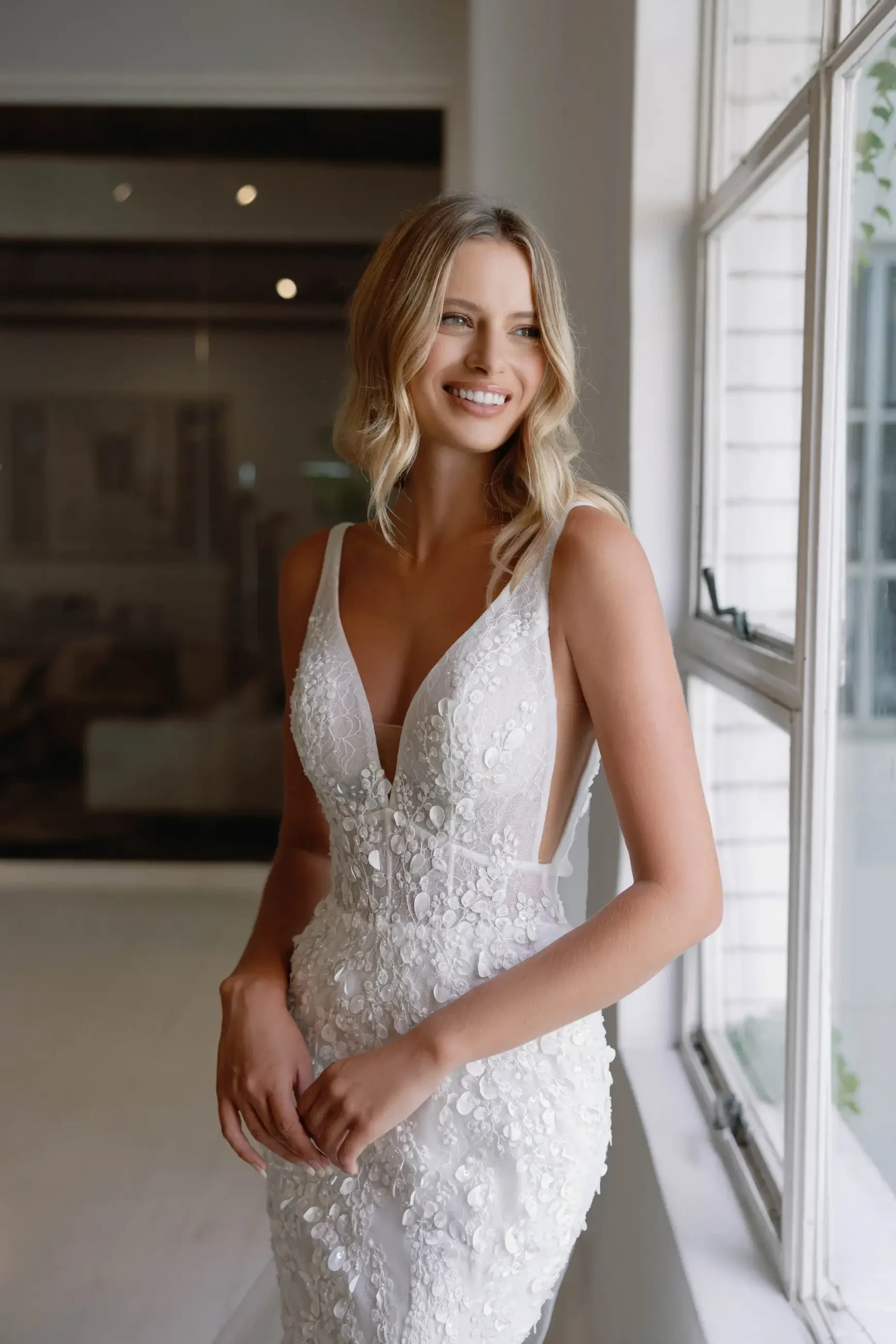 Model is wearing a sleeveless lace fit-and-flare gown featuring a low open back and subtle floral detailing.