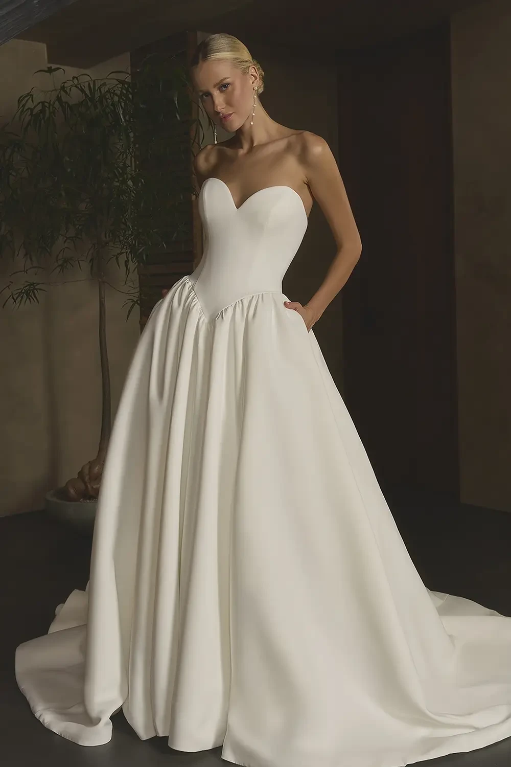 A model wearing a strapless white wedding gown with a sweetheart neckline and a voluminous skirt.